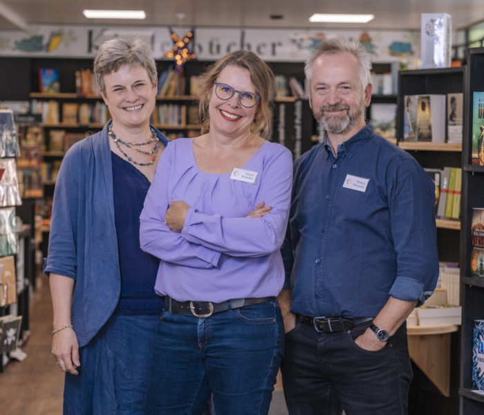 Zwei Frauen und ein Mann stehen in einer Buchhandlung.