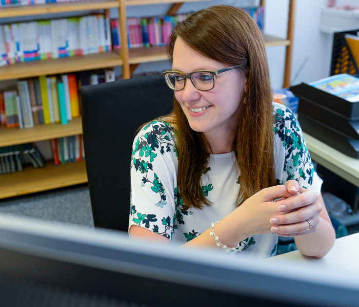 Frau sitzt vor Bildschirm an einem Schreibtisch.