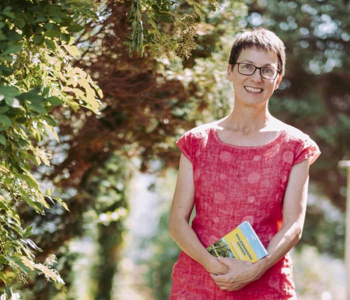 Annette Sievers läuft lächelnd mit Buch durchs Grüne.