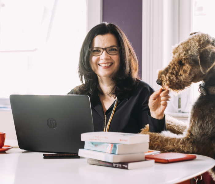 Charlotte Taylor sitzt vor einem Laptop und füttert einen Hund, der neben ihr sitzt.